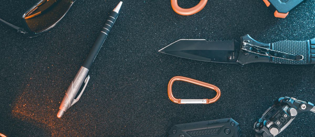 Flat lay of essential EDC gear featuring a pen, knife, sunglasses, and more on a textured background.