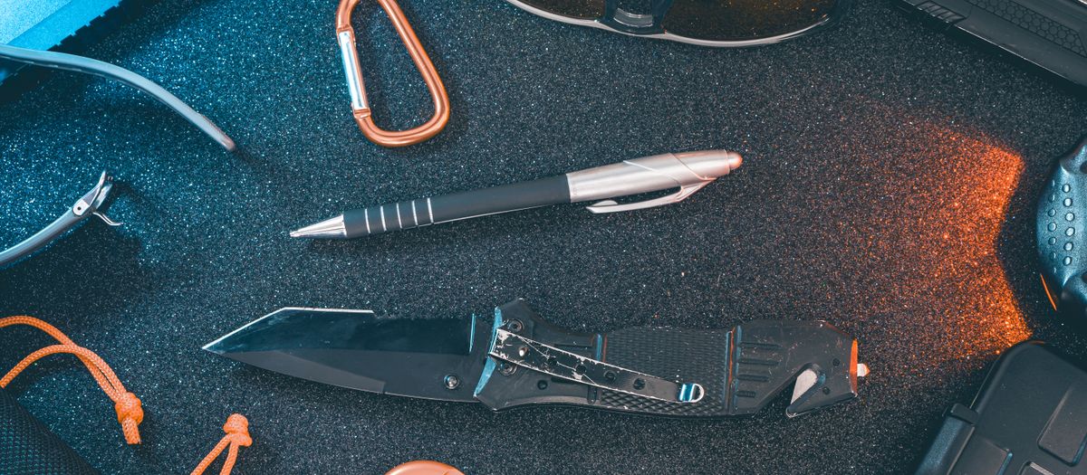 A flat lay of essential everyday carry items including a knife, pen, sunglasses, and carabiner.