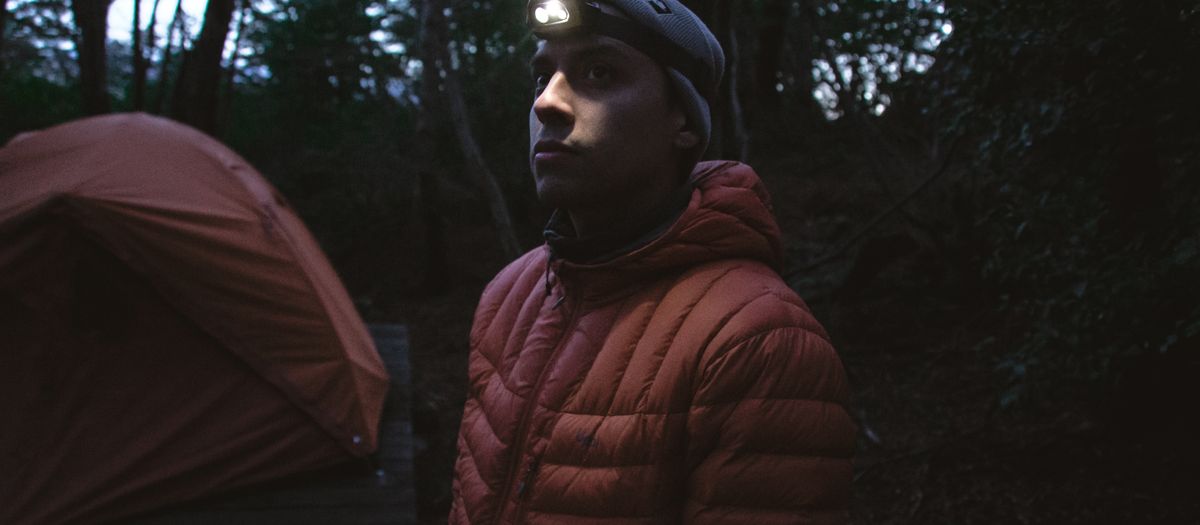 A man with a headlamp in a forest at night, near a tent in Torres del Paine.