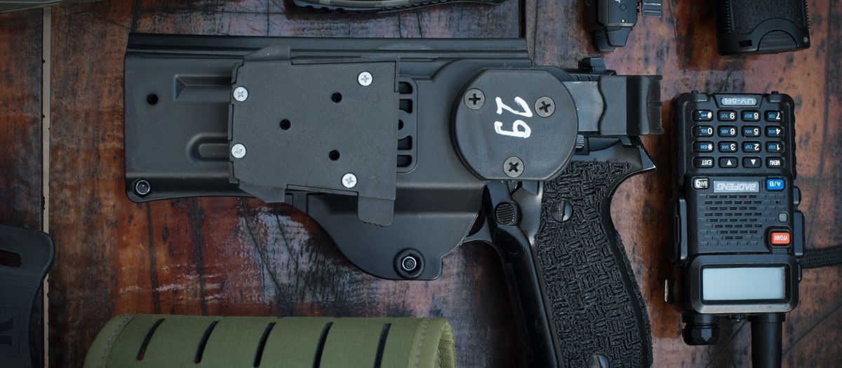 Flat lay of tactical gear including a pistol, radio, flashlight, and knife, set on a wooden surface.