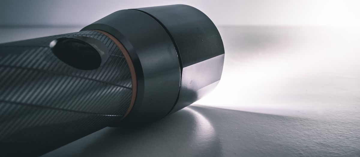 A close-up image of a metallic flashlight illuminated, highlighting its sleek design against a dark background.