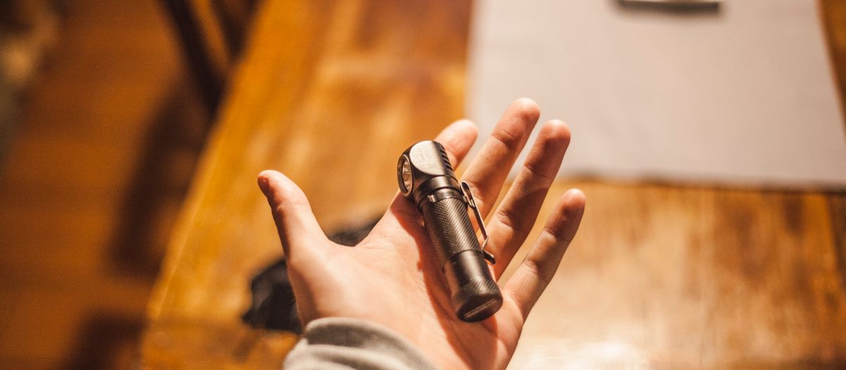 Close-up of a hand holding a flashlight on a wooden table indoors, warm lighting.