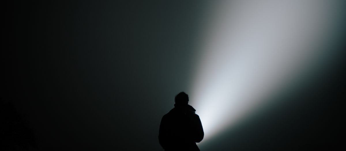 Silhouette of a person in dense fog, illuminated by a bright flashlight.