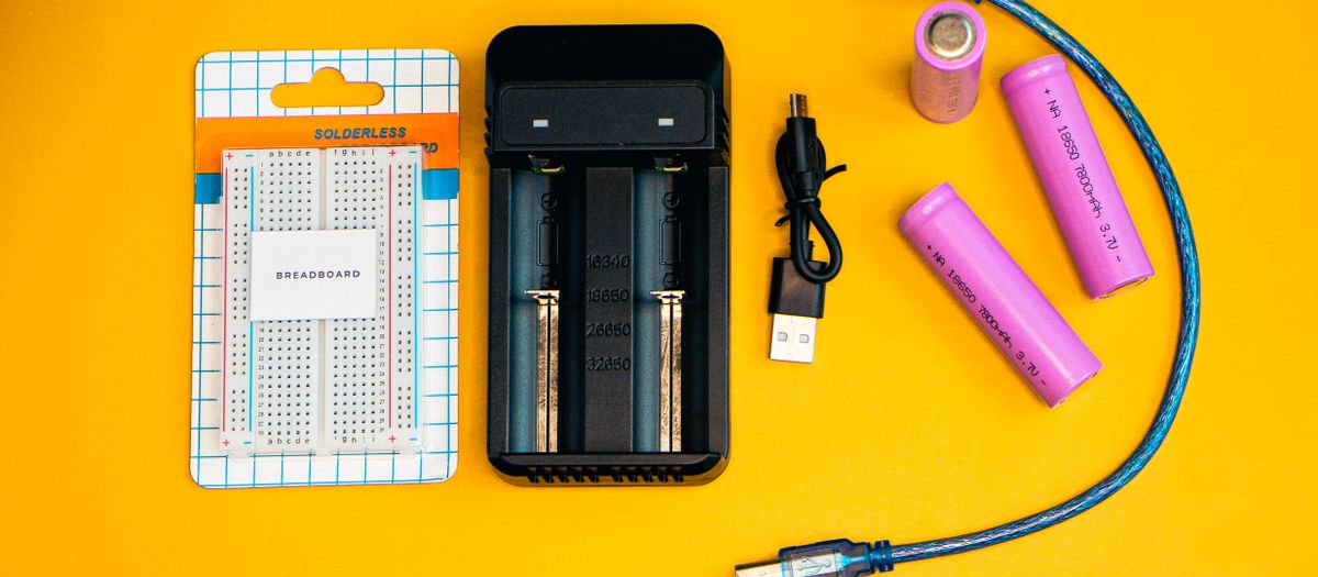 Flat lay of electronics including a breadboard and battery charger against a vibrant yellow backdrop.